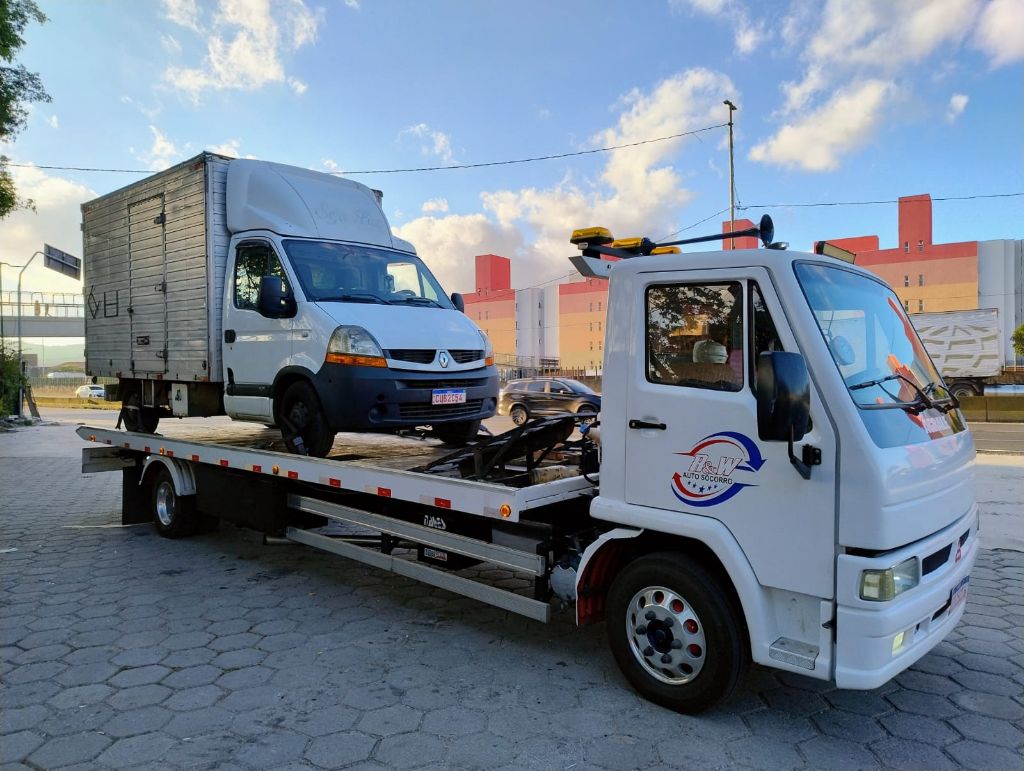Guincho plataforma transportando veículo utilitário branco